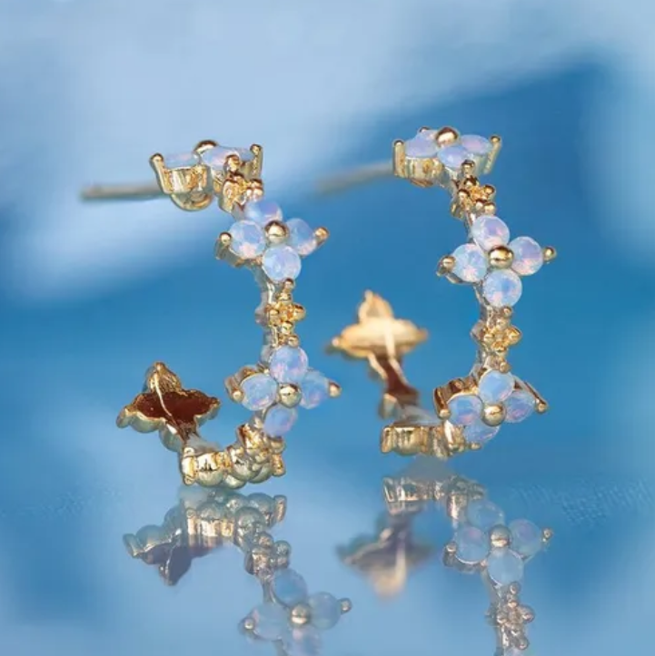 Gold and blue floral hoop earrings on a reflective blue surface