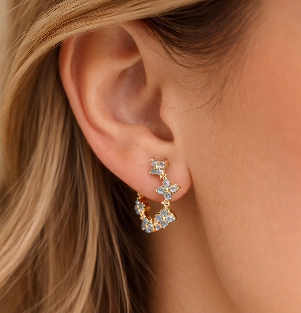 Close-up of an ear wearing a gold earring with blue gemstones.