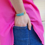 Person wearing a turquoise and gold beaded bracelet on a pink fabric background