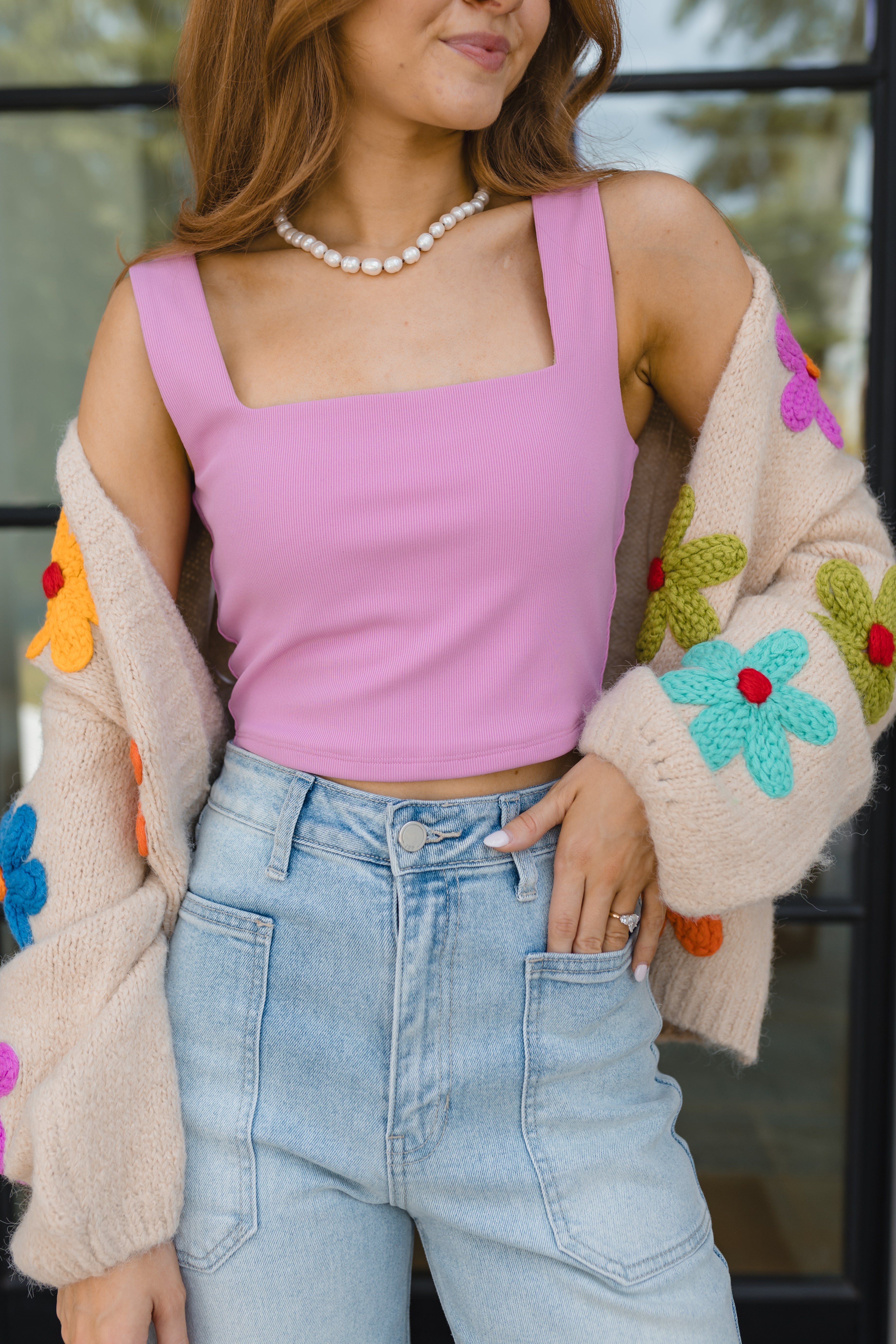 Woman wearing a light pink tank top and a flower cardigan with a pearl necklace