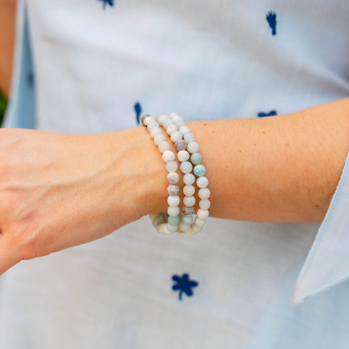 Picture of model's wrist with three beaded bracelets with white marbled and light blue beads.
