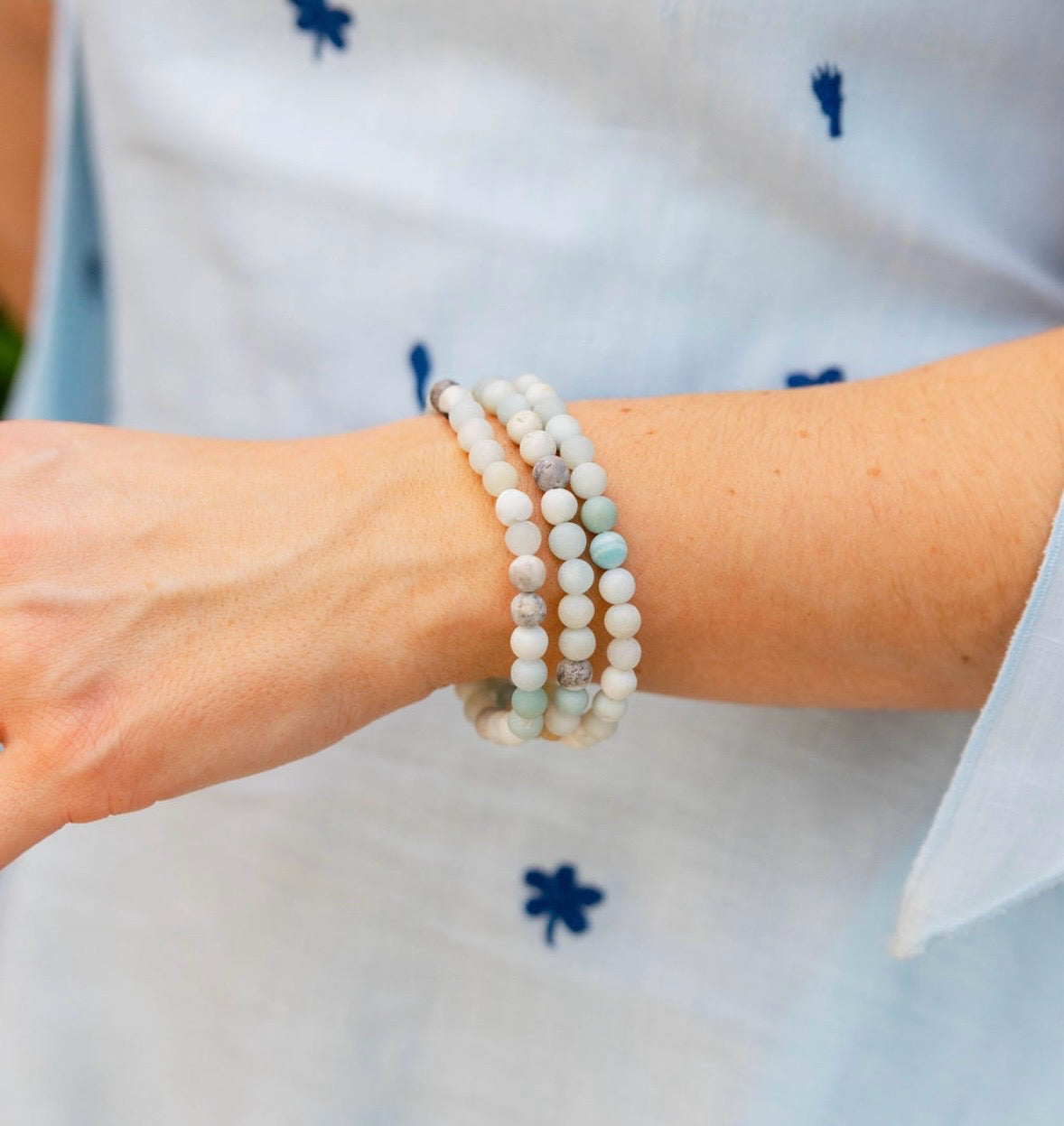 Picture of model's wrist with three beaded bracelets with white marbled and light blue beads.