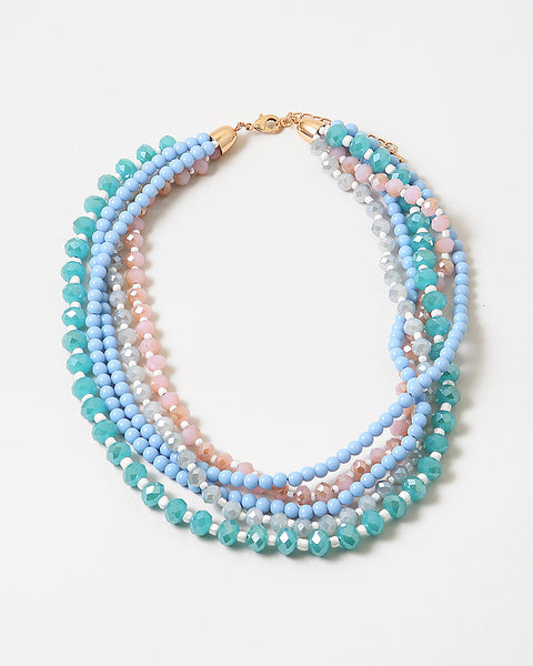 An image of layered beaded necklaces (blue, green, and pink) stacked on each other