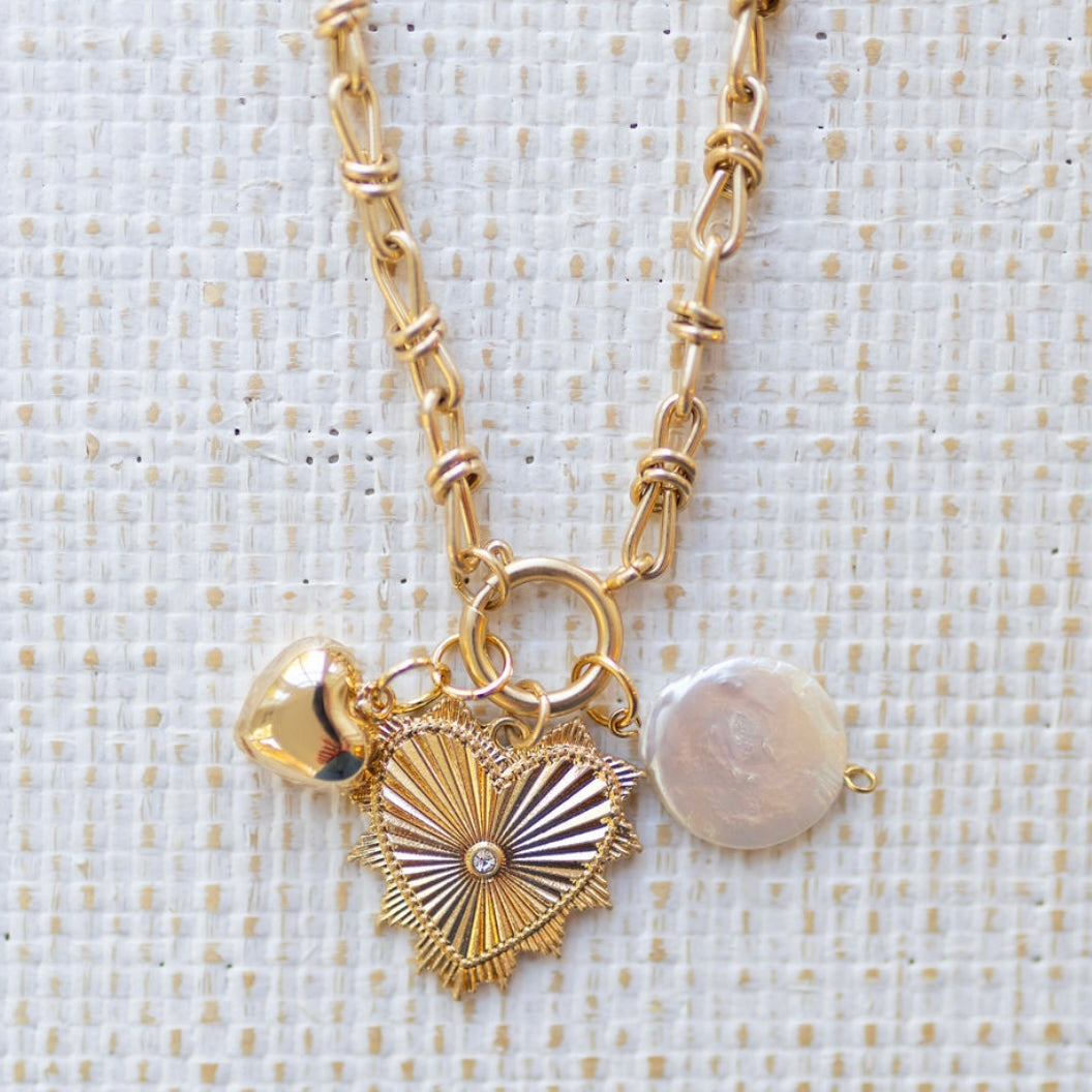 Picture of gold toggle chain with a large gold heart pendant with a diamond in the center, a bubble gold heart and pearl disc charm.