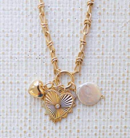 Picture of gold toggle chain with a large gold heart pendant with a diamond in the center, a bubble gold heart and pearl disc charm.