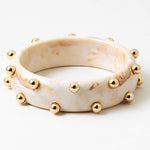 Picture of a marbled ivory colored bangle with inlaid gold beads.