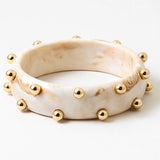 Picture of a marbled ivory colored bangle with inlaid gold beads.
