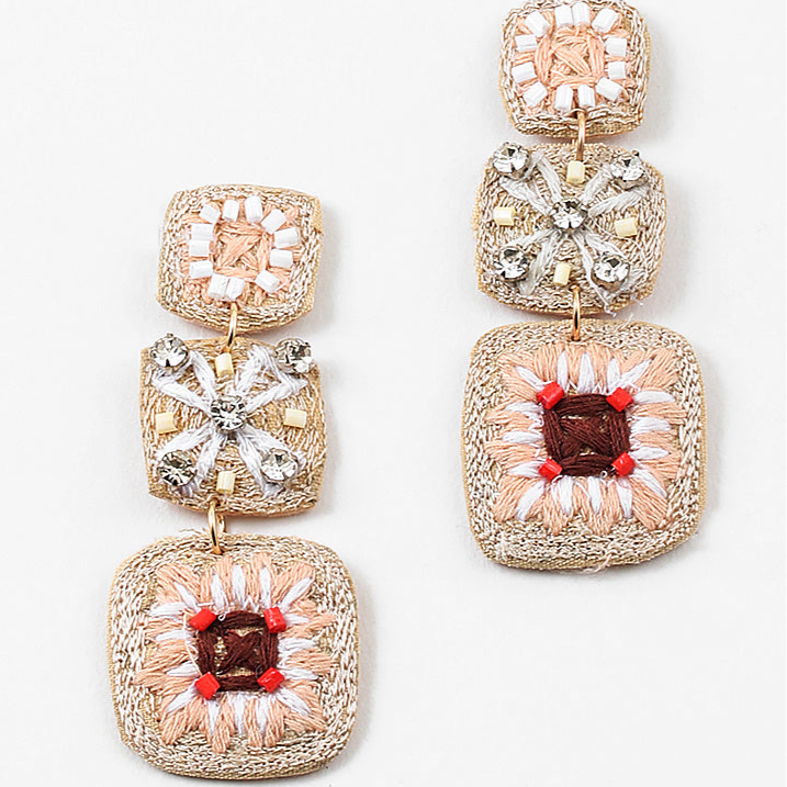 A set of dangle earrings with three sections. Top square is woven in beige with white beads, the second is a beige woven square with white string and clear stones and the third section is a woven square with beige, white and brown strings and pink beads.