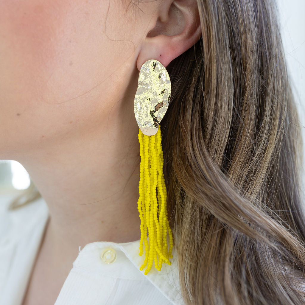 Picture of a large gold hammered oval disc  earring with 6 shoulder length yellow strands.