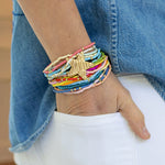 Colorful beaded bracelet set with a gold star charm on a wrist, wearing denim jeans and white pants.