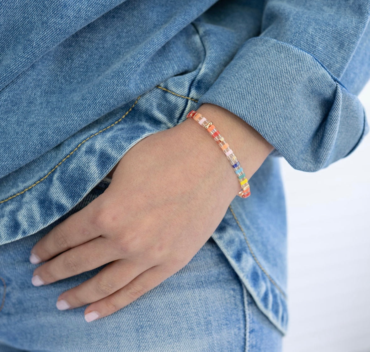 Person wearing a colorful rectangle bead bracelet with a denim jacket