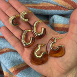 Gold and amber hoop earrings held in a hand with a striped fabric background