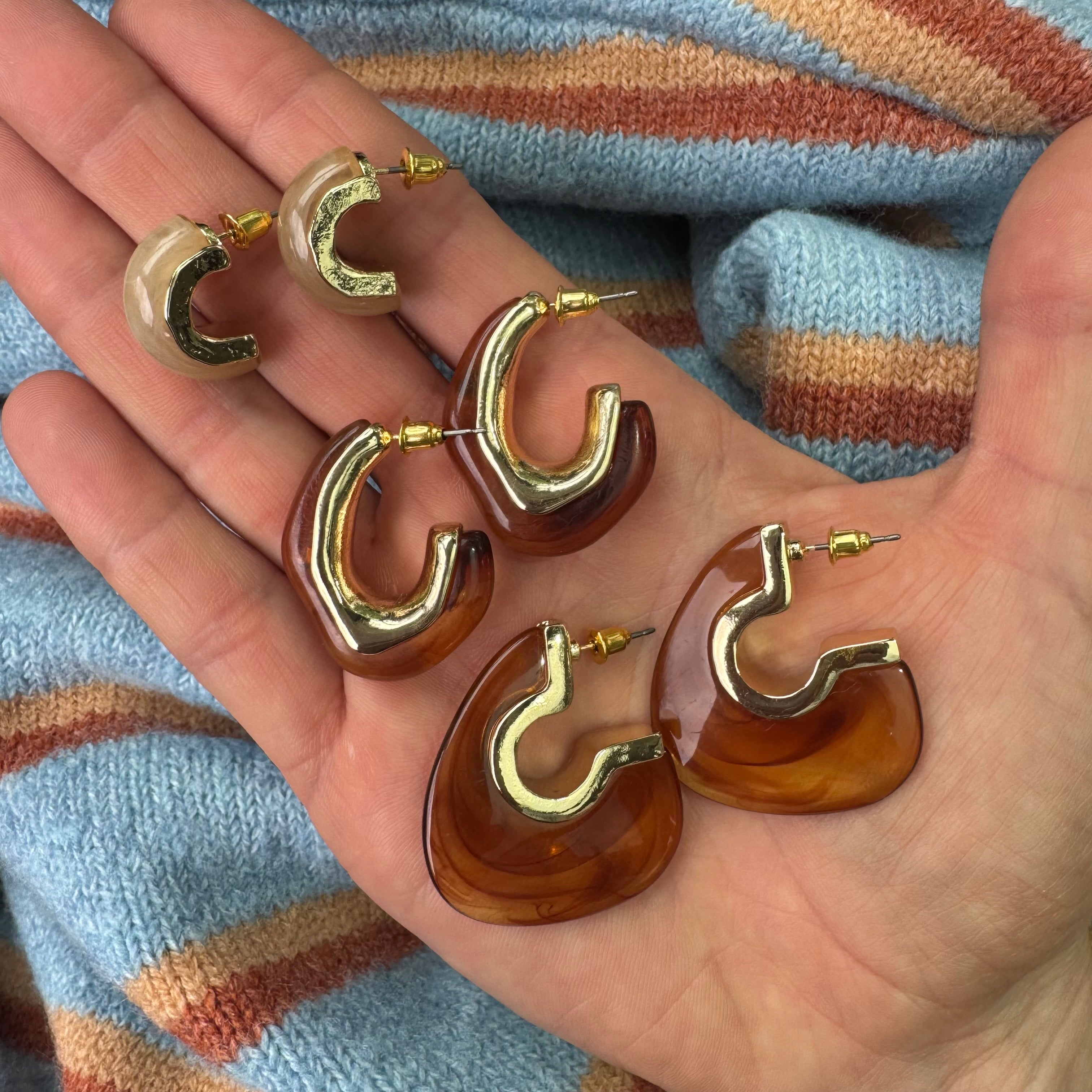 Gold and amber hoop earrings held in a hand with a striped fabric background