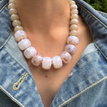 Necklace with large white beads worn by a person in a denim jacket.