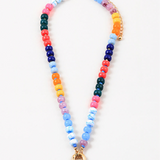 Picture of a bead necklace with a thick gold toggle clasp at its center. Beads are light blue, dark blue, orange, green, orange and yellow.