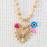 Picture of gold toggle chain with a large gold heart pendant with a diamond in the center. Three charms featured are a blue bead with a white and red flower, a pink lightening bold and pink heart stone charm.