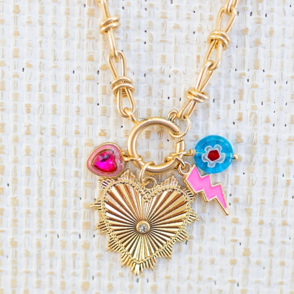 Picture of gold toggle chain with a large gold heart pendant with a diamond in the center. Three charms featured are a blue bead with a white and red flower, a pink lightening bold and pink heart stone charm.