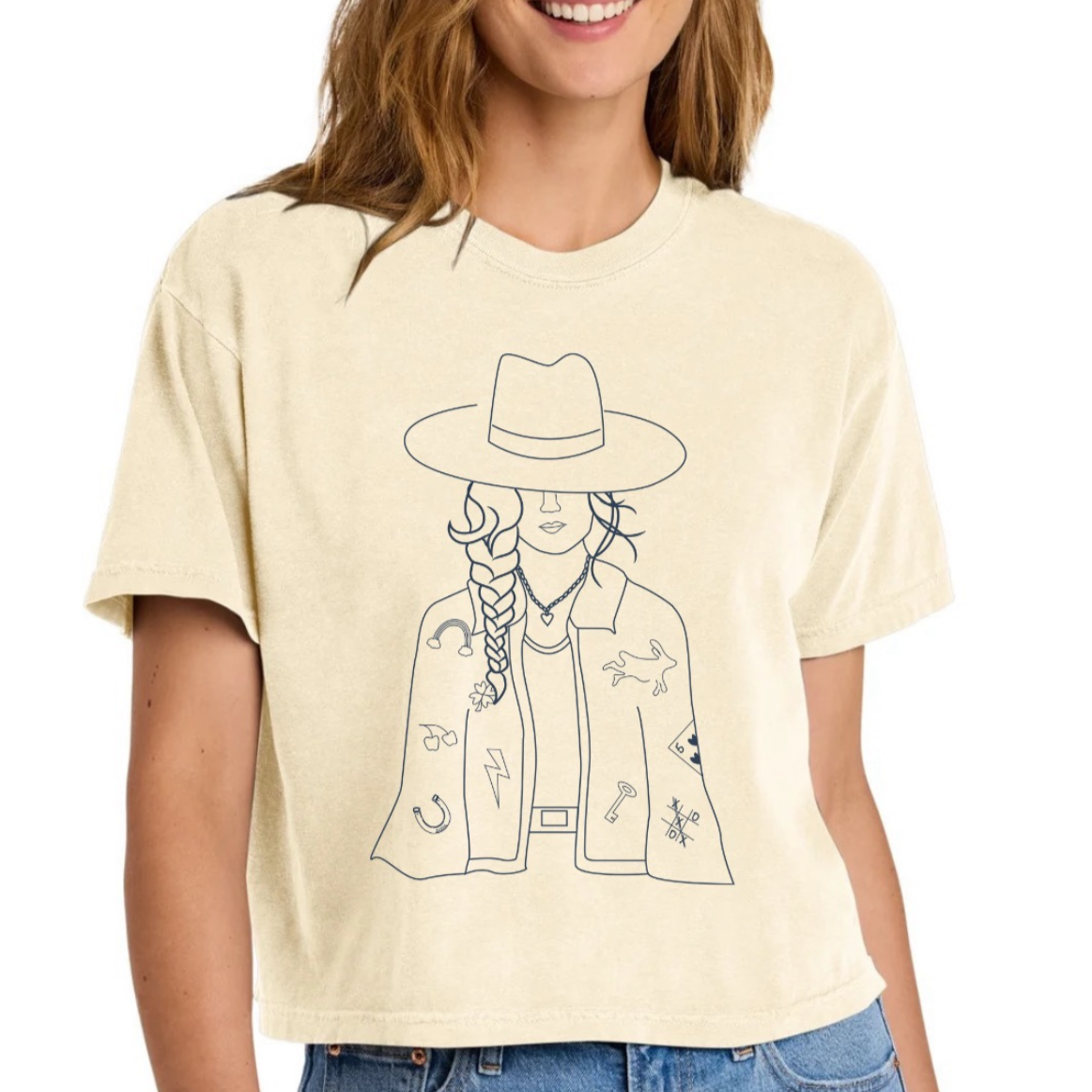 Person wearing a cream t-shirt with a graphic design of a person in a hat and jacket.