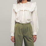 Picture of a model wearing a white long sleeved dress shirt. Shirt has a ruffle collar around the neck and breast and is a button up shirt.
