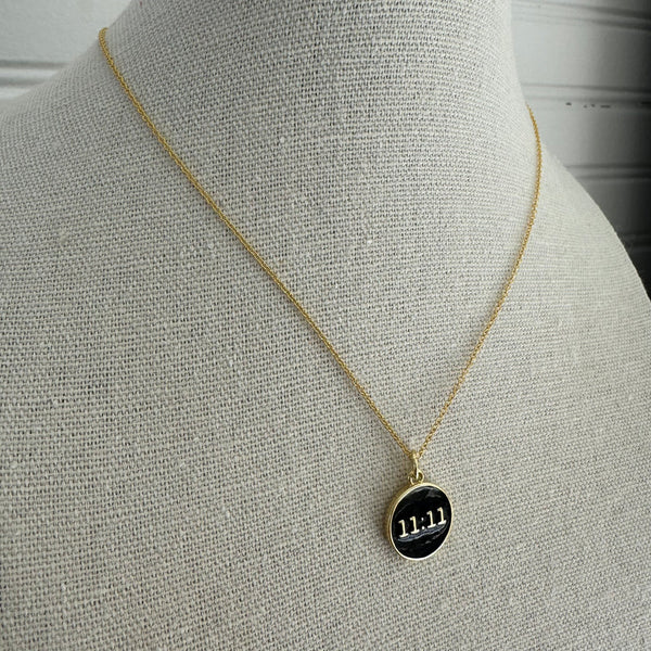 Picture of a fine gold chain necklace with a black disc 11:11 pendant.