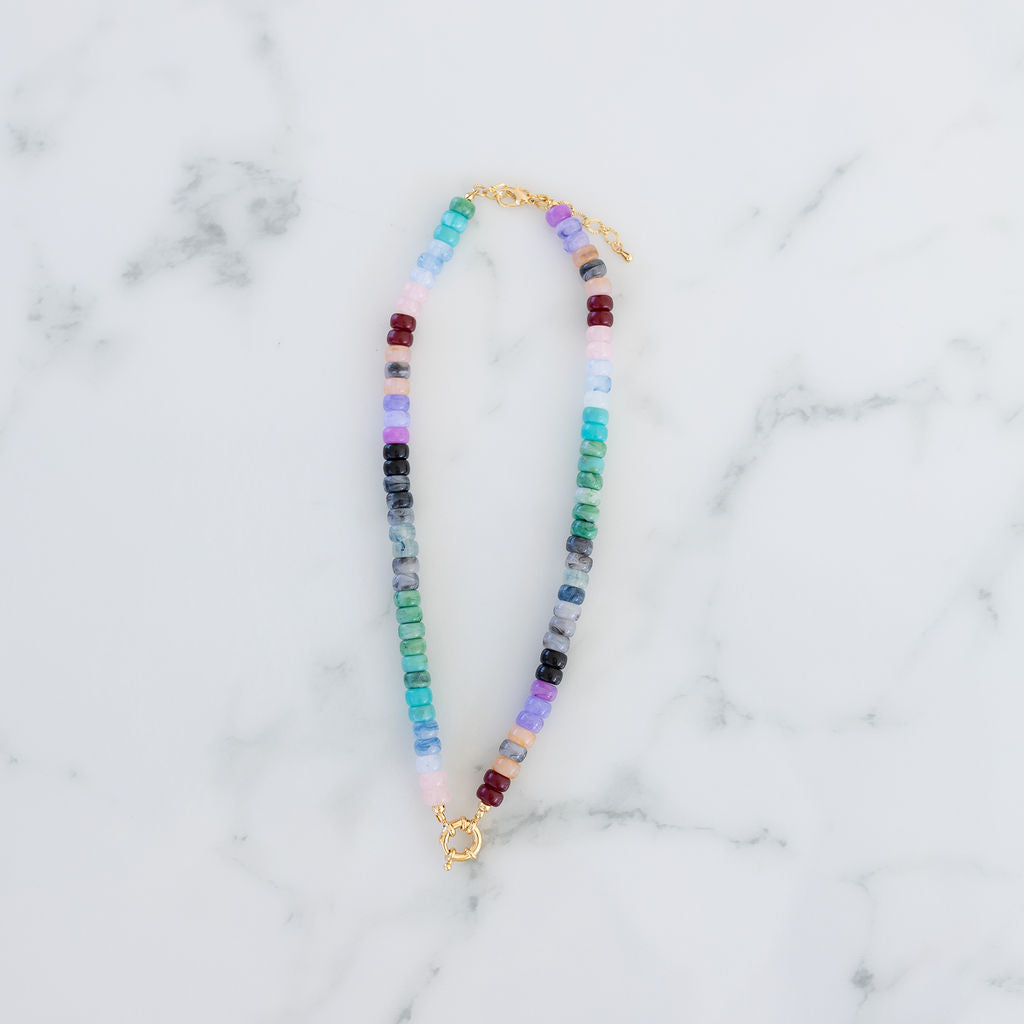 Picture of a multicolored bead necklace in turquoises and purples with a central gold toggle clasp.