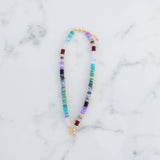 Picture of a multicolored bead necklace in turquoises and purples with a central gold toggle clasp.
