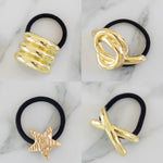 Four gold hair tie holders on black hair ties against a marble background