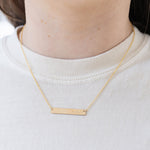Picture of model wearing a fine gold chain with a bar pendant.