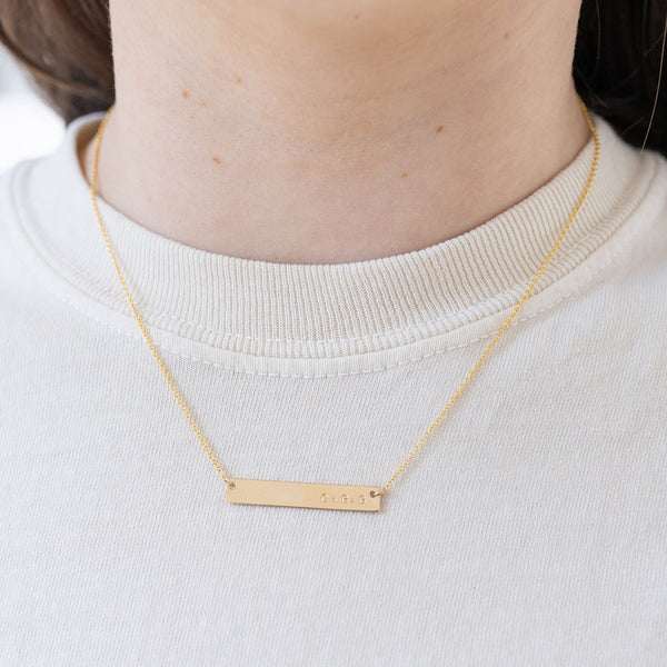 Picture of model wearing a fine gold chain with a bar pendant.