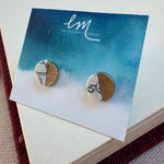 Picture of a pair of studs in a blue and white earring holder. Earrings are half white and black marble and half textured gold.