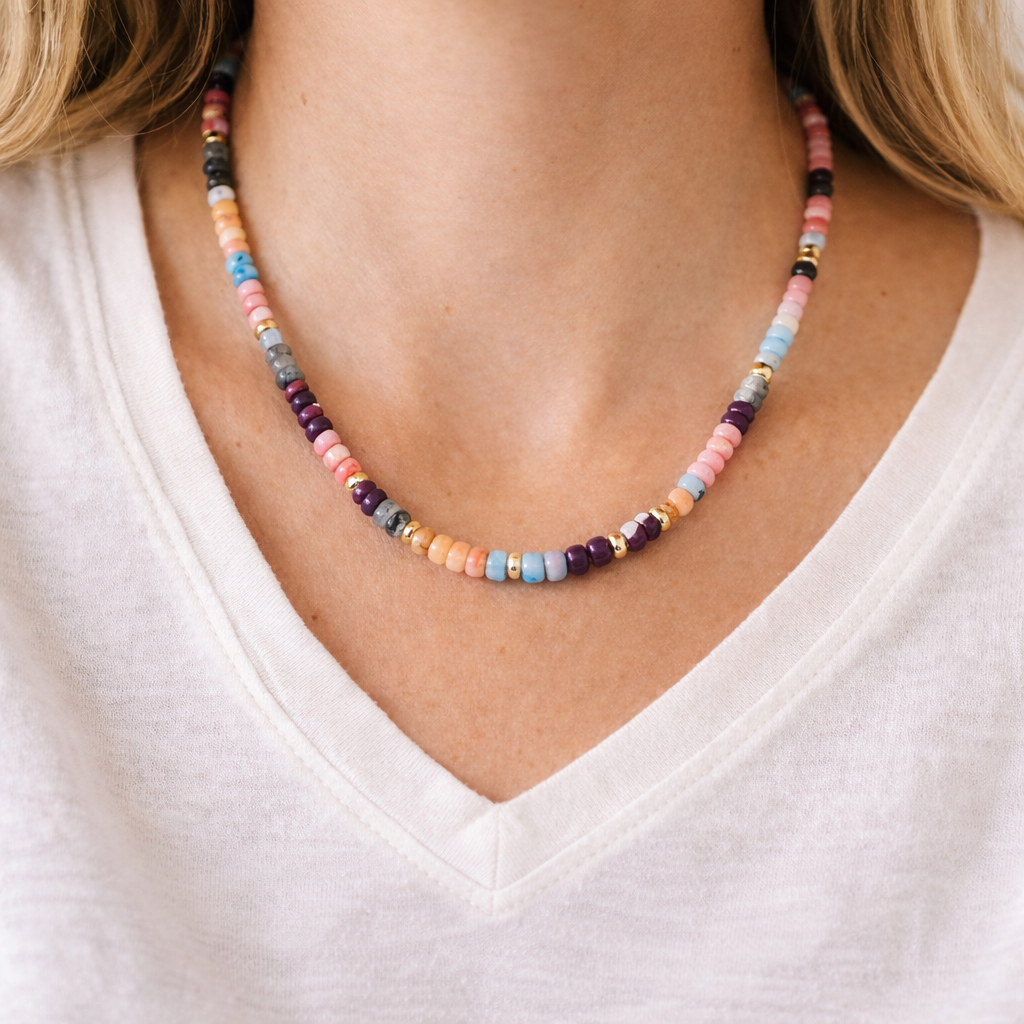 Multicolored beaded necklace in pinks, corals , reds and blues on a person wearing a white shirt