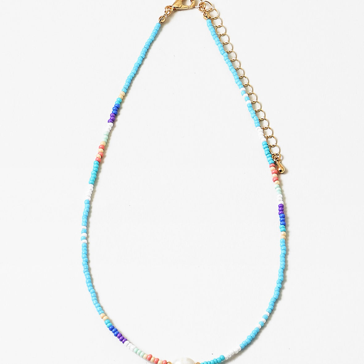 Necklace with different shades of blue beads and gold chain with a fresh water pearl on a white background