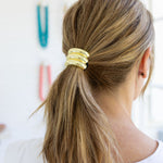 Woman with a ponytail wearing a gold hair tie against a blurred background