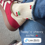 Screenshot of crossed legs wearing jeans and red sneakers. Socks are cream colored with small cherries on them.