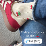 Screenshot of crossed legs wearing jeans and red sneakers. Socks are cream colored with small cherries on them.