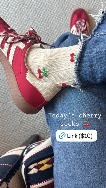 Screenshot of crossed legs wearing jeans and red sneakers. Socks are cream colored with small cherries on them.