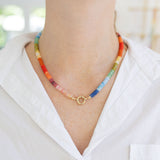 Picture of a brightly colored necklace with a central gold clasp. Beads are orange, yellow, pinks, blues and greens.