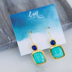 Gold earrings with blue and green stones on a branded card