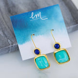 Gold earrings with blue and green stones on a branded card