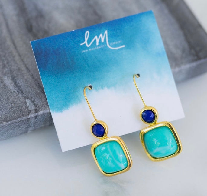 Gold earrings with blue and green stones on a branded card