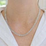 Necklace with small clear beads worn by a person in a white shirt