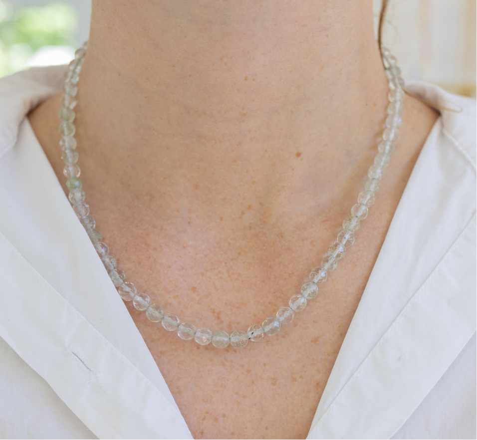 Necklace with small clear beads worn by a person in a white shirt