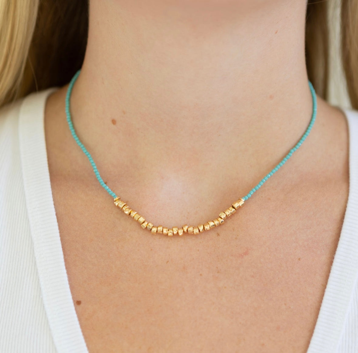 Blue and gold beaded necklace on a person wearing a white top