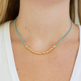 Blue and gold beaded necklace on a person wearing a white top