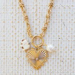 Picture of gold toggle chain with a large gold pendant with a diamond in the center. Attached are two charms, one a white elephant and one a fresh water pearl.