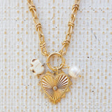 Picture of gold toggle chain with a large gold pendant with a diamond in the center. Attached are two charms, one a white elephant and one a fresh water pearl.