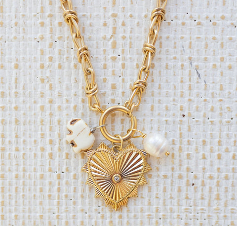 Picture of gold toggle chain with a large gold pendant with a diamond in the center. Attached are two charms, one a white elephant and one a fresh water pearl.