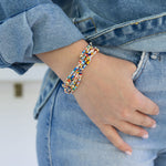 Picture of a woman's hand in her front pocket. She is wearing 6 dainty bracelets made of tiny multicolored seed beads.