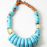 Chunky statement necklace with blue beads and a brown cord on a white background