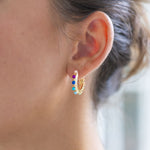 Woman wearing white hoop earrings with colorful gemstones on it